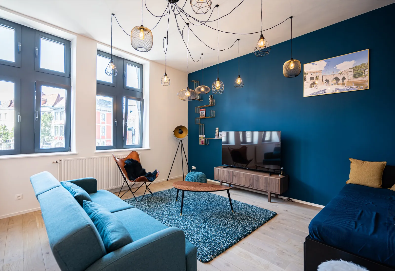 Salon bleu canard avec suspensions, canapé et télévision dans l'appartement de la Camuche Peterinck, gîte à Tournai