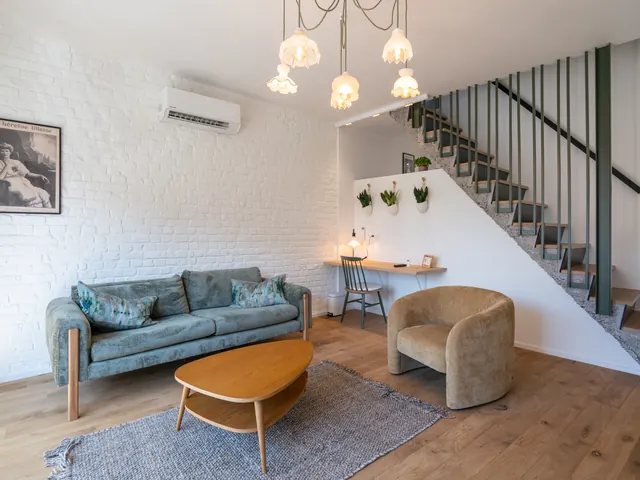 Séjour avec canapé vert, fauteuil en velours moutarde, table basse en bois et bureau sous l'escalier à garde-corps vert, suspension à abat-jours en verre opalin, Camuche de Bettignies à Tournai