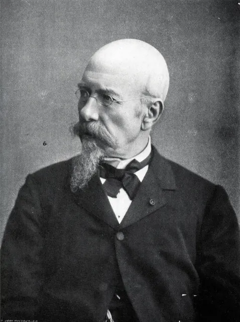 Portrait photographique d'Henri Beyaert âgé : crâne dégarni, lunettes, moustache et barbiche, de trois quarts, en costume sombre et nœud papillon, archive
