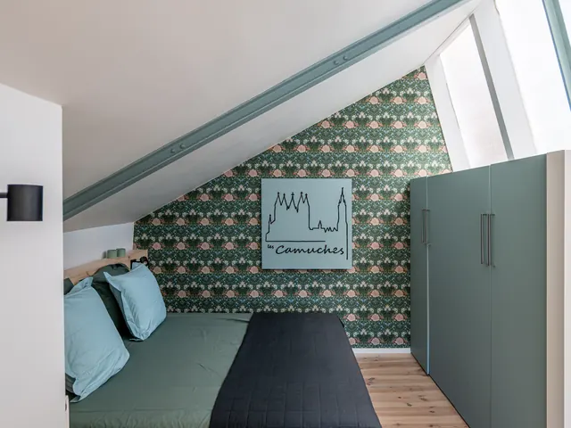 Lit contre un papier peint végétal vert, armoire verte et poutre métallique sous combles, Camuche Beyaert à Tournai