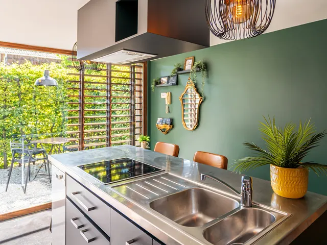 Cuisine aux meubles noirs, plan de travail en inox et mur vert, ouverte sur le patio, Camuche Beyaert à Tournai