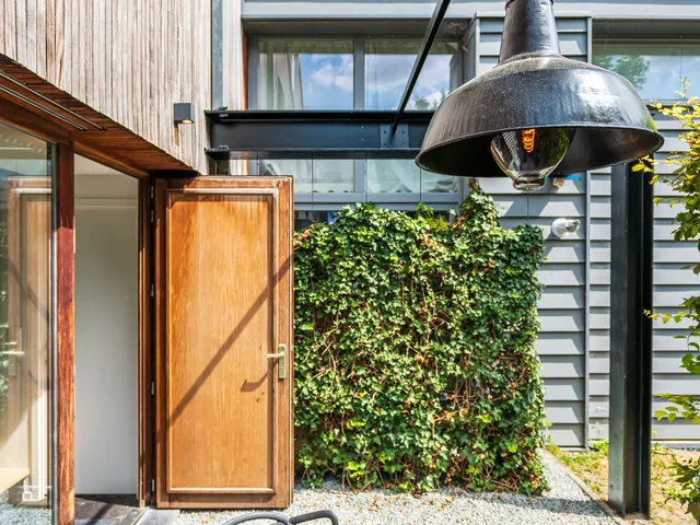 Patio de gravier avec suspension industrielle noire et porte en bois ouverte, Camuche Beyaert à Tournai