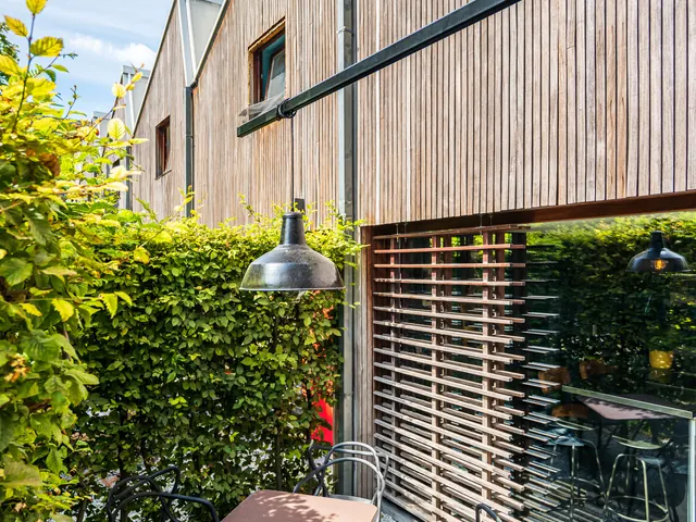 Patio avec table de bistrot et chaises noires devant la façade en bois et la haie, Camuche Beyaert à Tournai