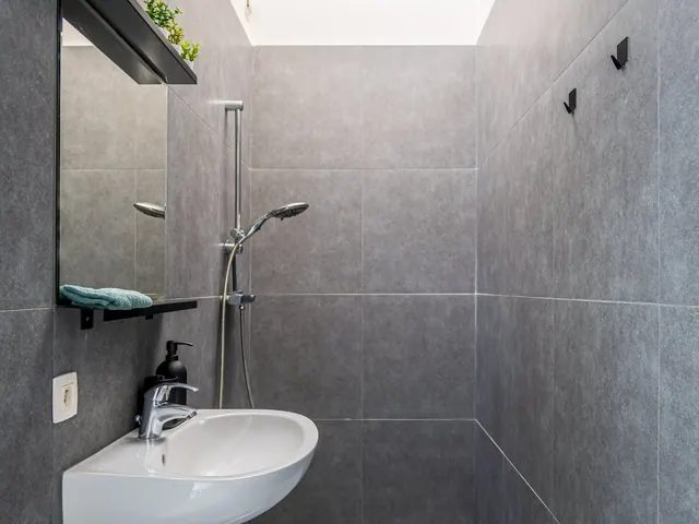 Salle de douche aux murs gris avec lavabo d'angle, miroir et lucarne zénithale, Camuche Beyaert à Tournai