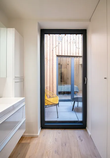 Patio habillé de bois et chaise Acapulco jaune, vu depuis la salle de bain, Camuche Boulenger à Tournai