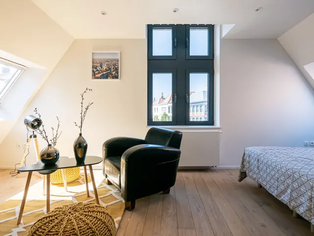 Pièce sous les combles avec fauteuil en cuir et grande fenêtre sur la ville, Camuche Desclée à Tournai