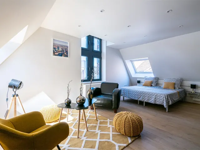 Séjour sous les combles avec fauteuil jaune, tapis et lit, duplex Camuche Desclée à Tournai