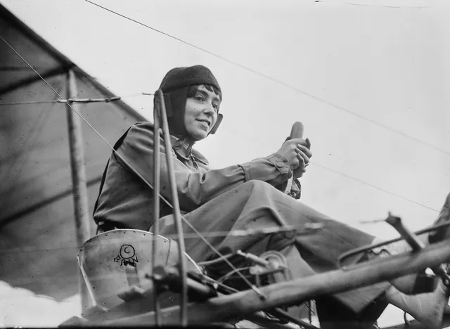Hélène Dutrieu souriante, en casque de cuir, les mains sur la commande d'un biplan, photographie ancienne, Camuche Dutrieu à Tournai