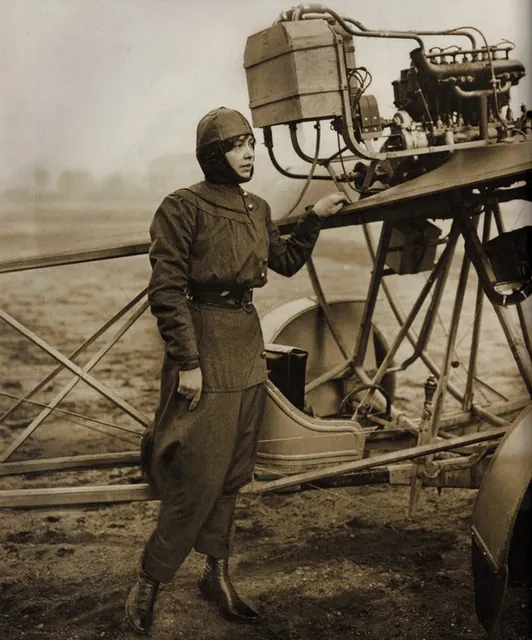 Aviatrice en combinaison et casque de cuir, debout près de son avion à moteur, photographie ancienne sépia redressée, Camuche Dutrieu à Tournai
