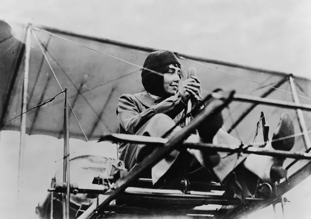 Hélène Dutrieu de profil, assise au poste de pilotage d'un biplan, les mains sur la commande, photographie ancienne, Camuche Dutrieu à Tournai