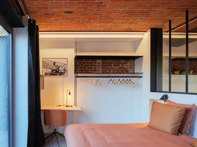Chambre avec penderie en métal noir devant un mur de briques, bureau en pin et photographie d'aviatrice, Camuche Dutrieu à Tournai