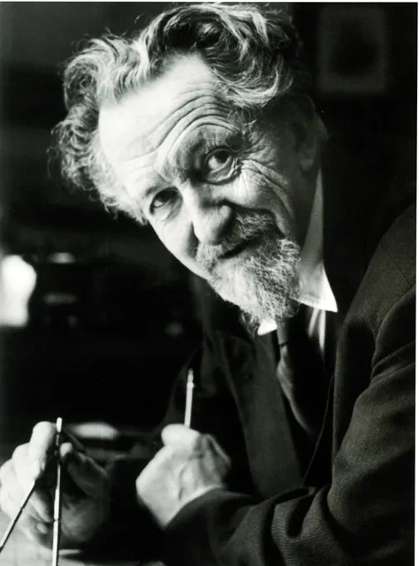 Portrait photographique d'Henry Lacoste âgé en noir et blanc : cheveux gris ébouriffés, barbe, regard levé, un crayon dans chaque main, archive