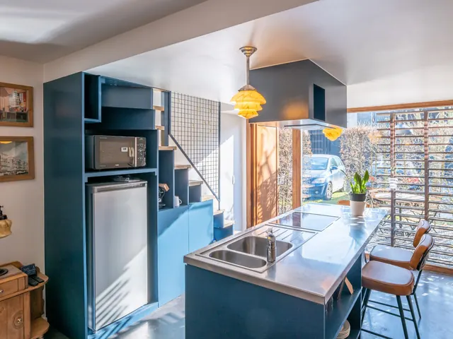 Cuisine avec îlot en inox, tabourets en cuir et grande baie coulissante sur le patio, Camuche Lacoste à Tournai